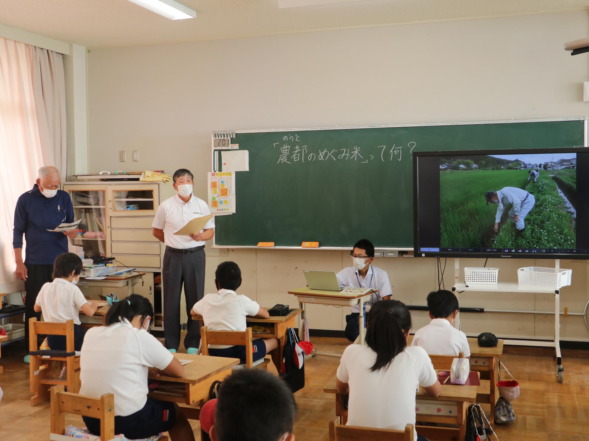 男性がスライドを使って農都のめぐみ米の説明をこどもたちにしている。