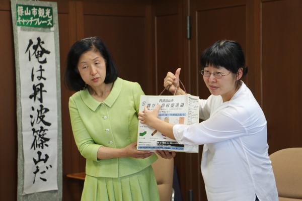 女性委員の方2名が可燃ごみ減量化のために作成された「雑がみ回収促進袋」を持って説明している写真