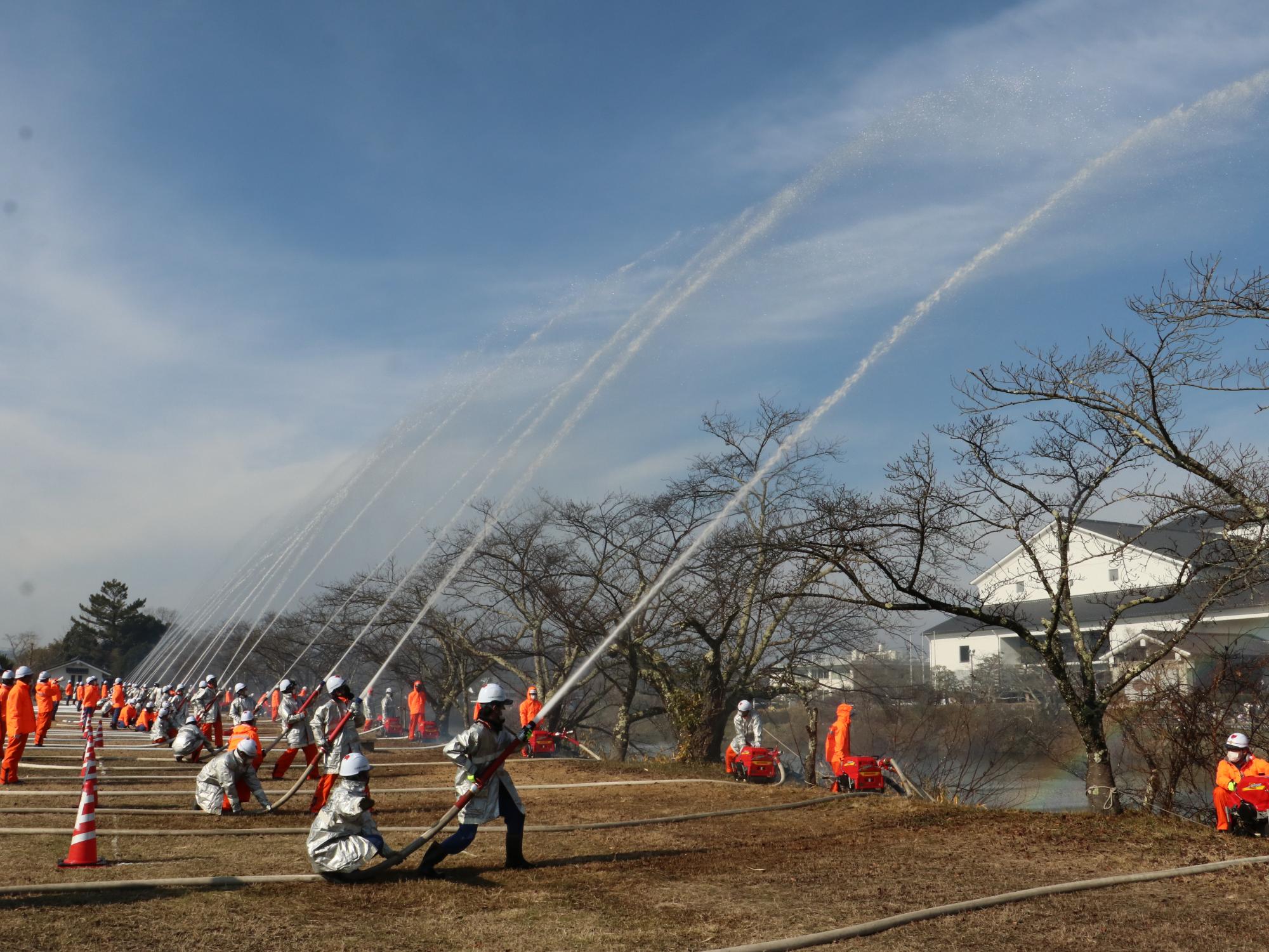 広場で、消防団の各分団の団員が放水している