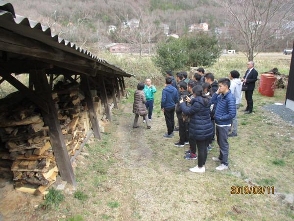 ブータンの若手行政官13人が薪が積まれている倉庫の前で説明を聞いている写真