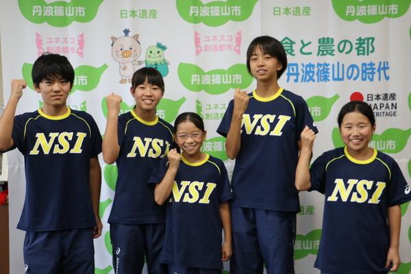 笑顔でガッツポーズをして並んでいる小稲君、東家さん、足立さん、北野さん、北川さんの写真