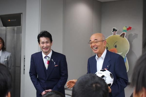 サッカーボールを片手に持った市長と紺色のスーツを着た男性が笑っている写真