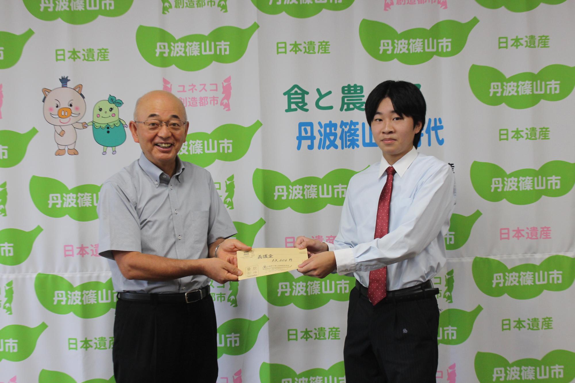 義援金が入った封筒を制服を着た男子高校生が市長に手渡ししている