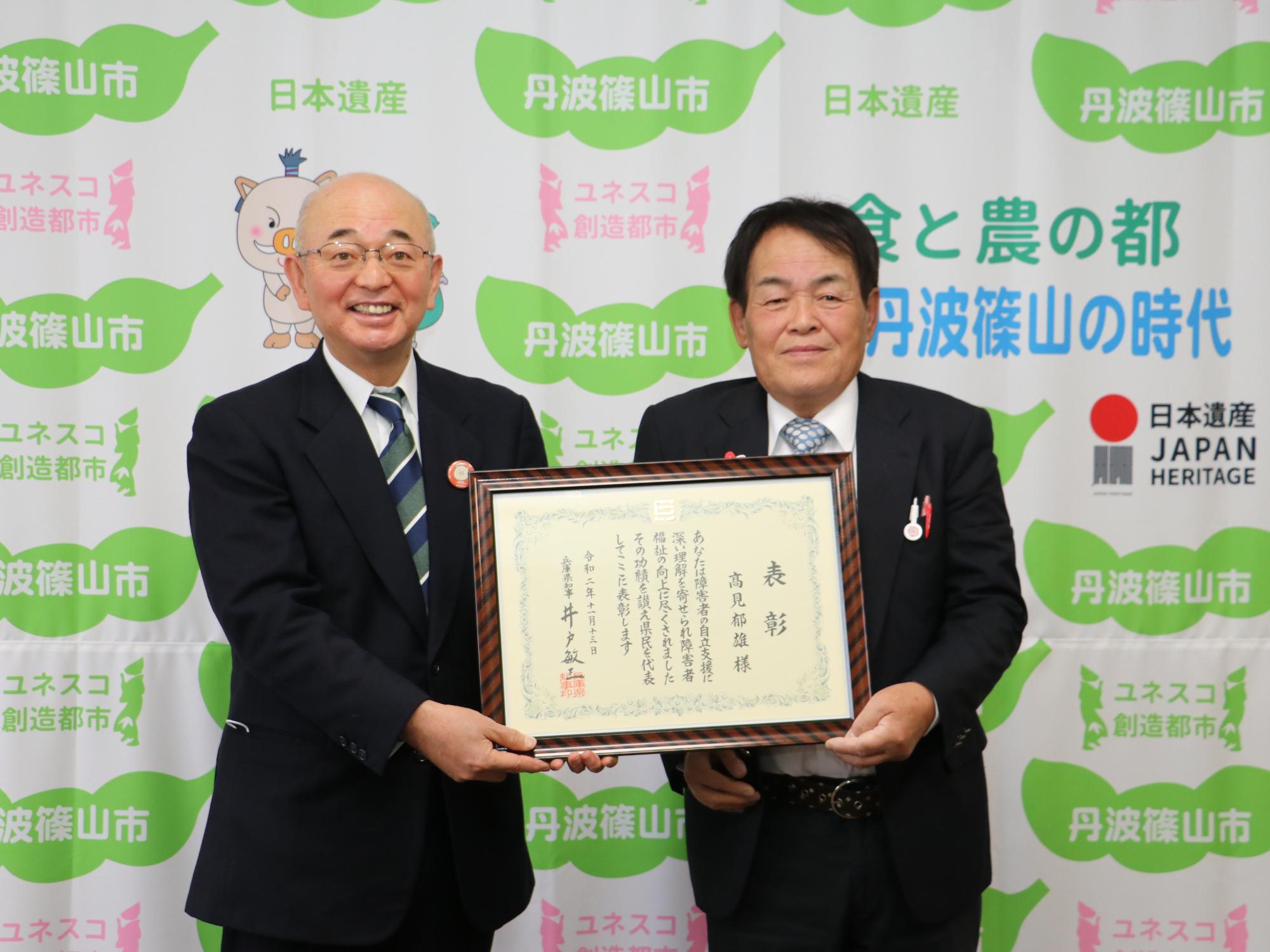 表彰状を市長と高見さんが二人で一緒に表彰状を手に持っている。