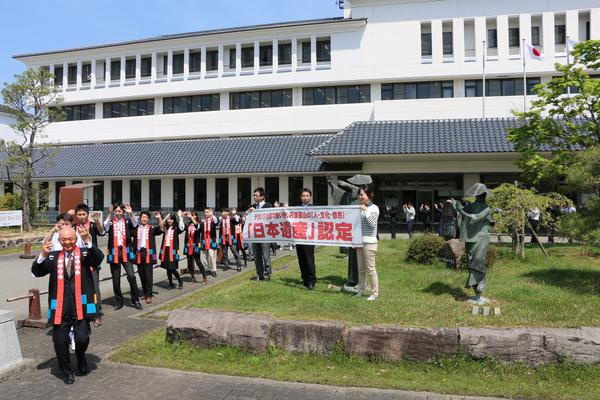 晴天の下、市長を先頭に法被を着た人々が、デカンショを踊っており、「日本遺産」認定と書かれている横断幕の横を踊り歩いている様子の写真