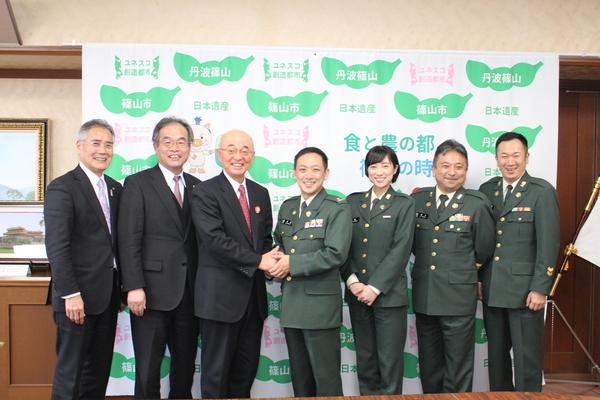市長と柴田隊長が握手をしており、柴田さんの隣に鶫さん、その横に2名の自衛官の方も一緒に写っている写真