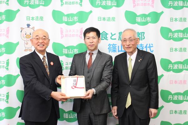 市長とその横の男性が目録を二人で持って立ちその横にもう男性がにこやかに並んでいる写真