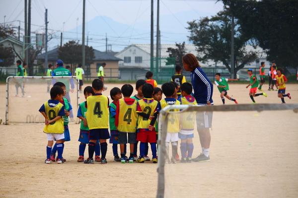 メッシュゼッケンベストを着た12人の少年たちが立っていて、ユニフォーム姿の北澤選手が少年たちに話をしている写真