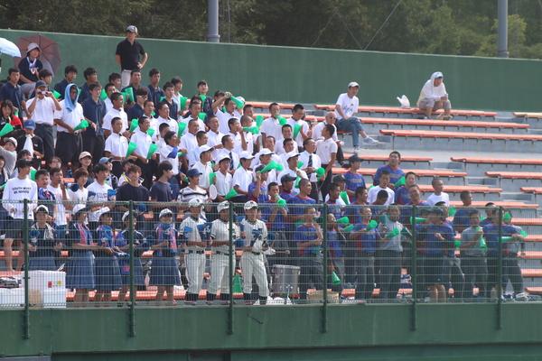 緑のプラスチックのメガホンを持った生徒と、応援に来た人たちがスタンド上で応援をしている写真
