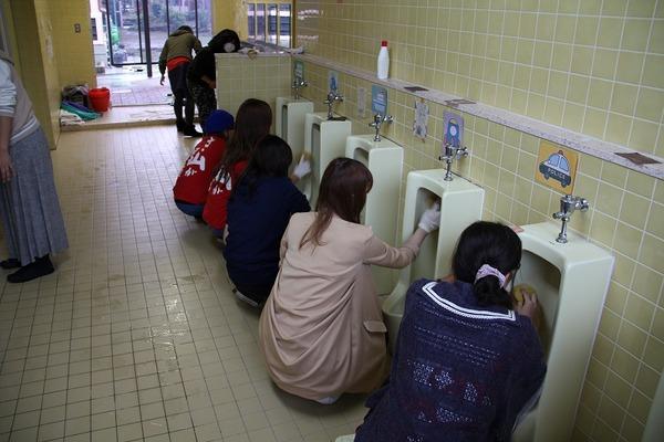 女性の参加者が男子トイレの便器を磨いている様子の写真