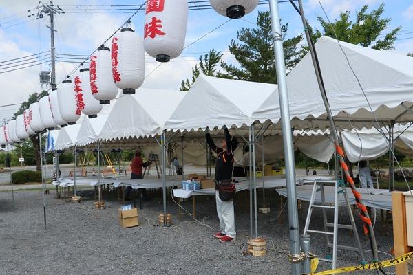 祭りの提灯とテントが設置された会場で作業をする女性らの写真