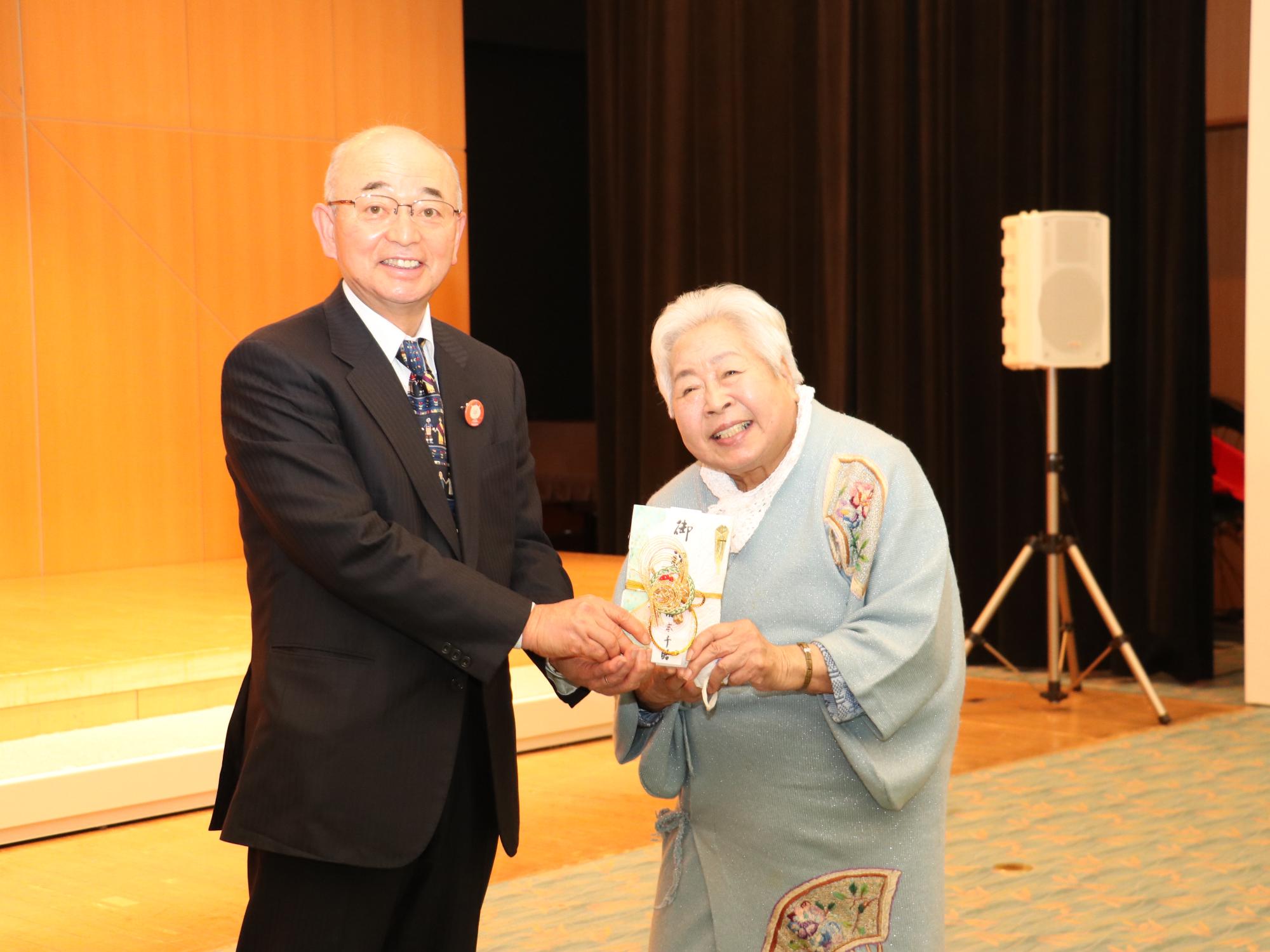 藤木氏が寄附金入りの封筒をえがおで市長に渡している