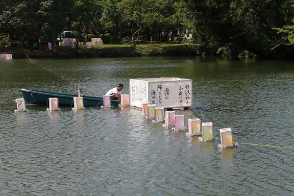 ボートに乗った男性が祭りの様々な灯篭を池に設置している写真