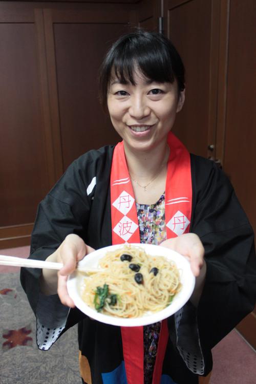 女性が「黒豆ビーフン（みそ味）」）を完成させて紹介している写真
