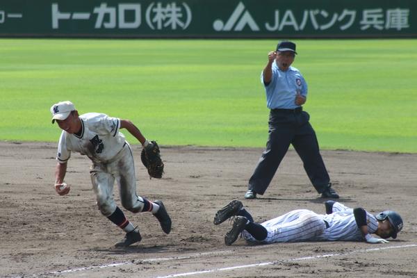 ベースに滑り込みしている相手チームの選手の横で、ボールを持ってどこかに走りだそうとしている篠山鳳鳴高校軟式野球部の選手と、うしろで、アウトのポーズをしている審判の写真
