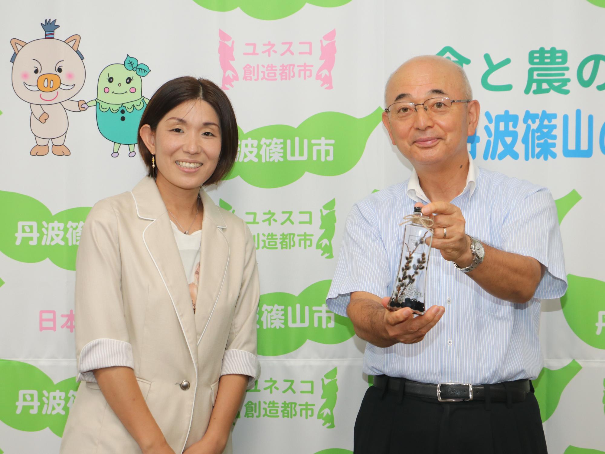 黒豆を使ったハーバリウムを手に持つ市長と、作者の女性の記念撮影