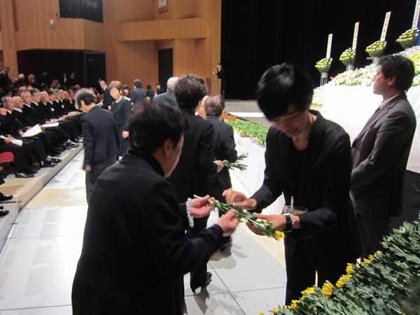 参列者たちが花を一輪ずつ受け取って、献花台に花を置いている写真