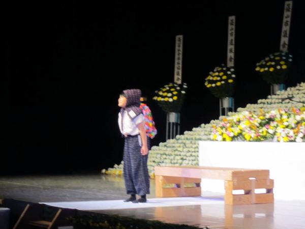 頭に防空頭巾をかぶった少女が舞台に立っている写真