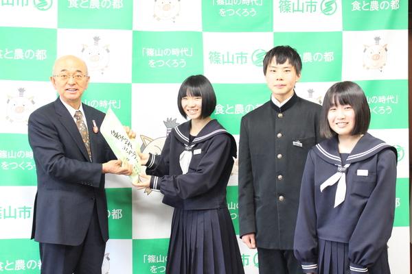市長が女子生徒より支援金を受け取っており、他の2名の生徒も笑顔で写っている様子の写真