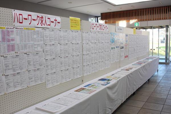 ハローワーク求人コーナーと書かれた掲示板に貼られた沢山の紙と、その前に置かれた机の上に並ぶ資料の写真