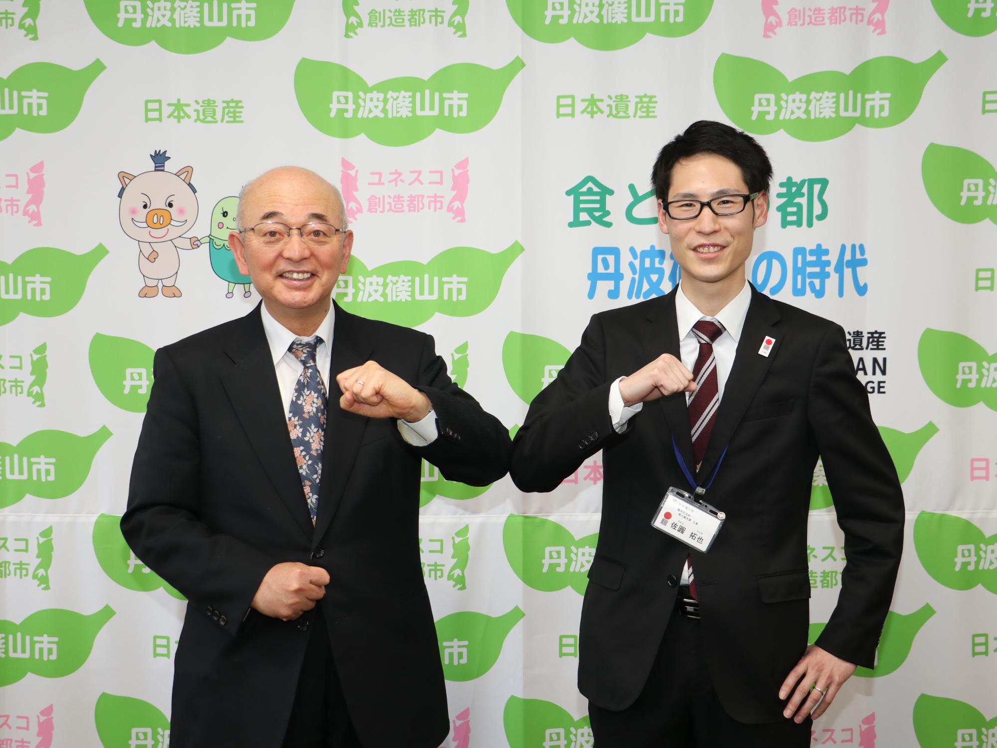 胸元にこぶしをあてて記念撮影している市長と男性職員