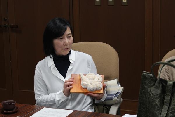 自身が手掛けた板の上に白い雲の様な作品を手にして説明しているほんいでん すみよさんの写真