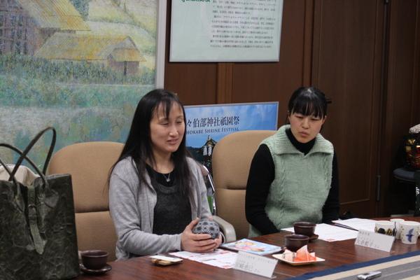 自身が手掛けたガラス細工で作った灰色の球体の形をして水玉模様のついた作品を手にして説明をしている宮崎 恵巳さんの写真