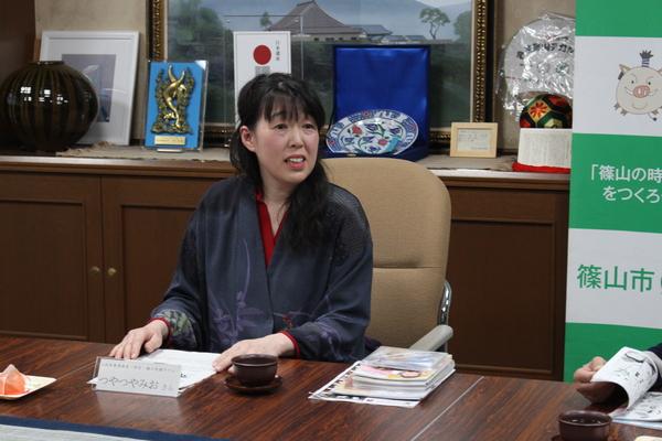 自身が書いた漫画やパンフレットなどの作品を目の前にして説明をしているつやつや みおさんの写真