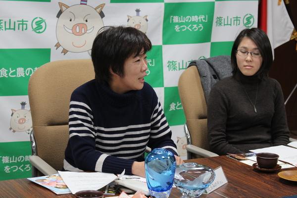 吹きガラスで作られた透明な水色の2種類の花瓶を目の前に説明をしている児玉 みのりさんの写真