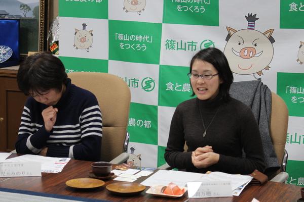 自身が手掛けた木材で作られたお皿2枚の前で説明している岸田 万穂さんの写真