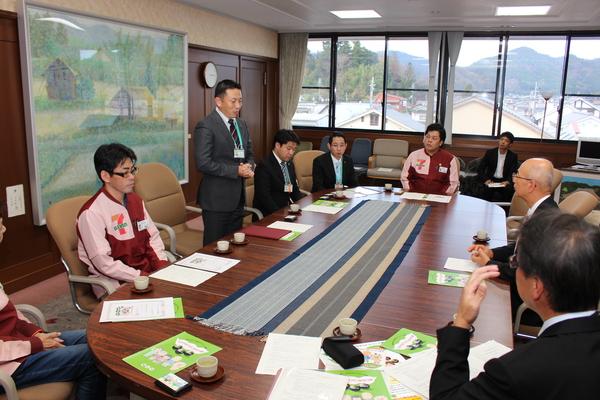 男性が話をされていて、株式会社セブン‐イレブンの制服を着た方と数名が座っている写真