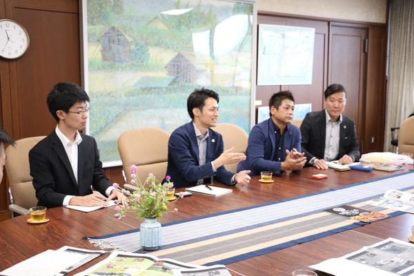 スーツをきた男性が4名座っていて、左から2番目の男性が話をしている写真