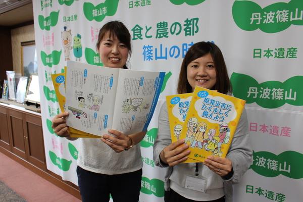 完成した原発災害に備えるハンドブックを女性職員2名が手に持っている写真