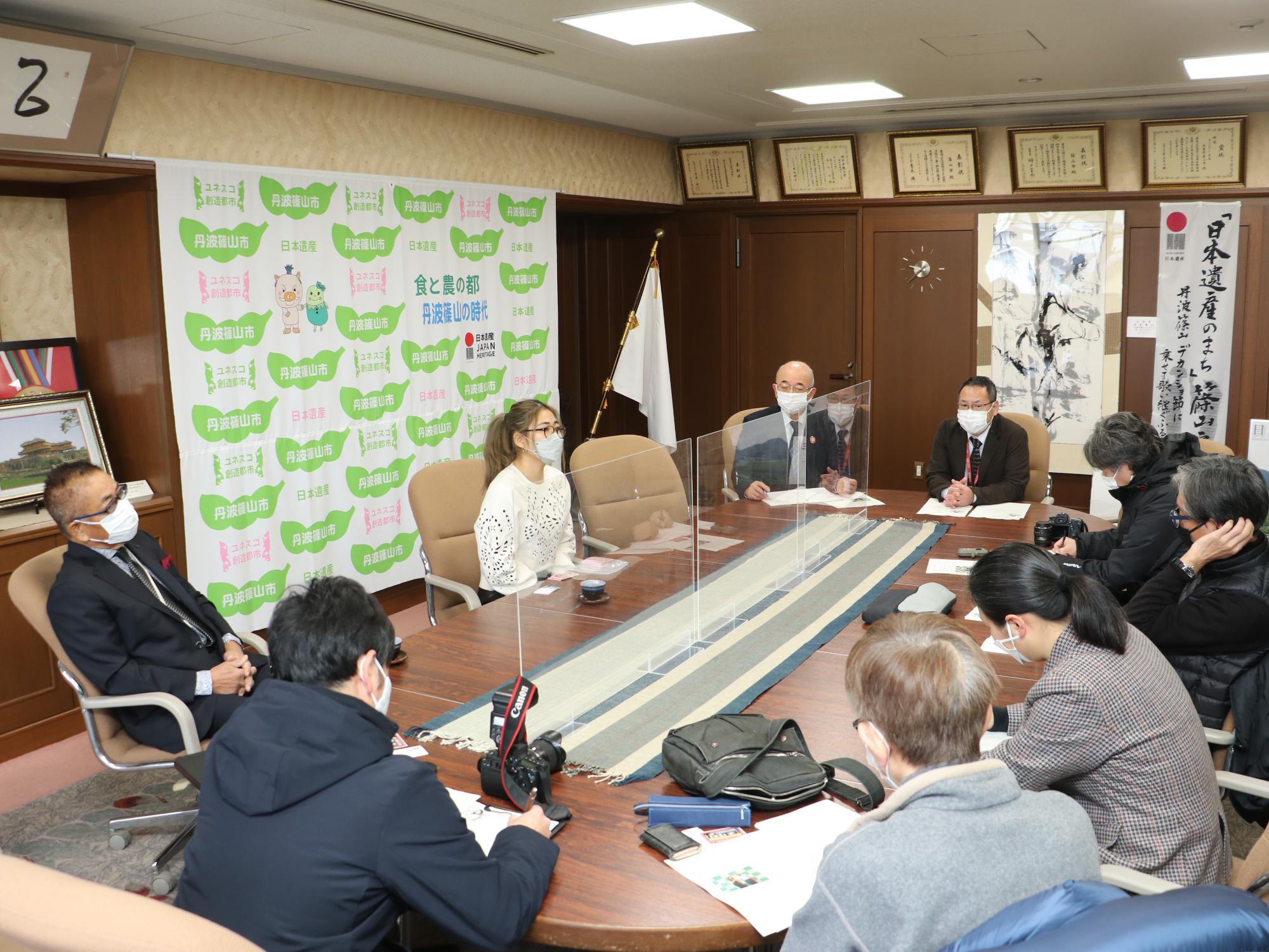 表敬訪問に来られた女性と、記者、市長、職員が話をしている