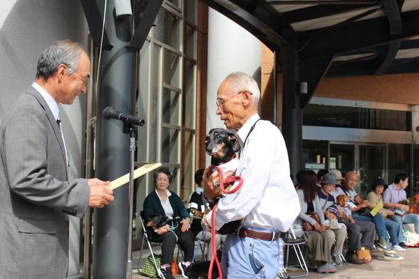 長寿犬を抱っこした飼い主の方が表彰されている写真