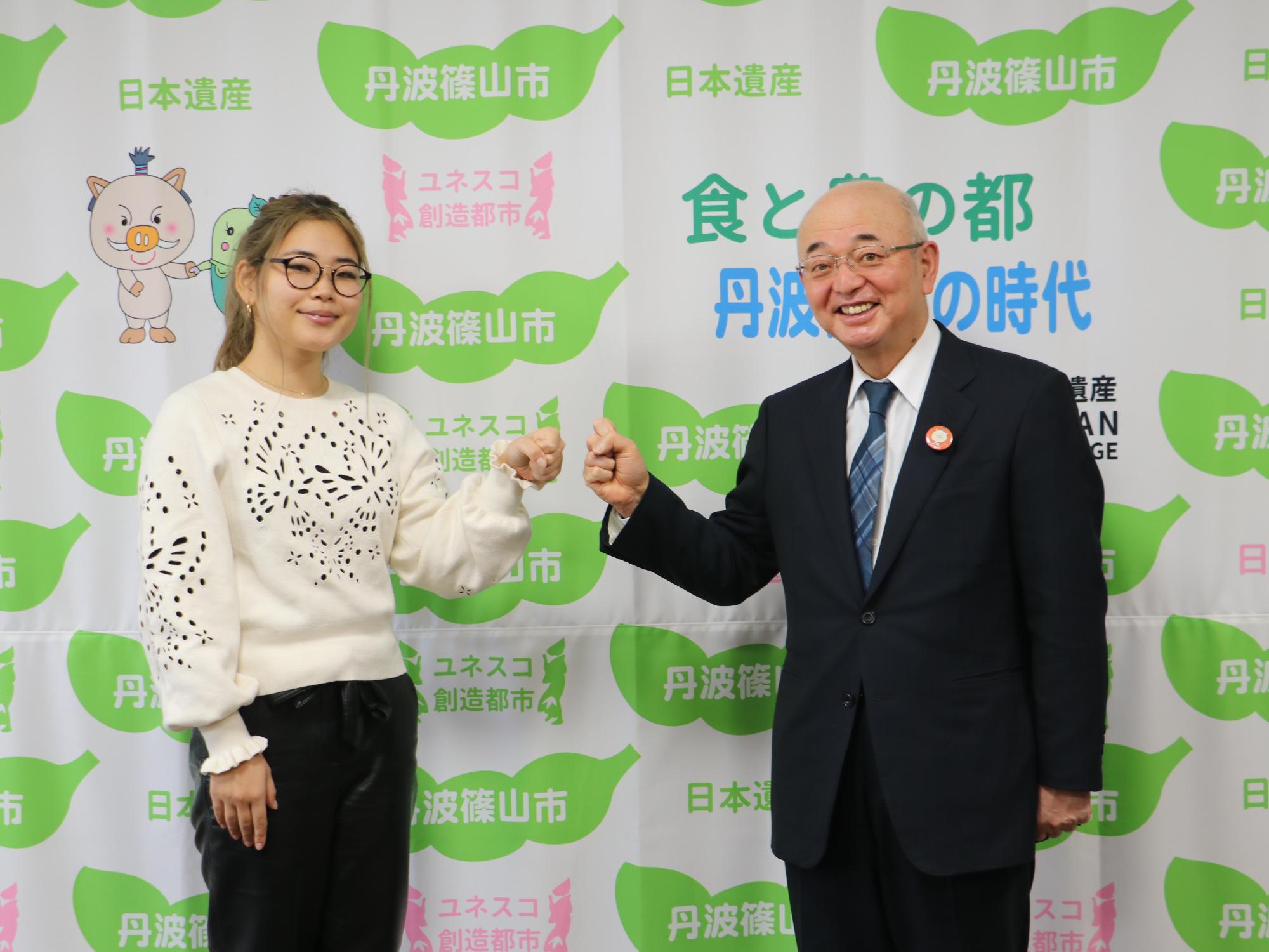 表敬訪問に来られた女性と市長がグータッチを使用としている