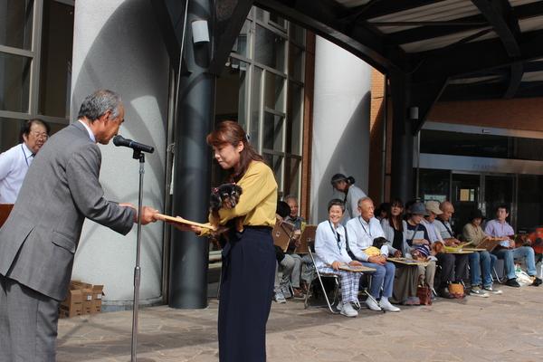 耳にリボンをつけた長寿犬が飼い主の方に抱かれ表彰されている写真