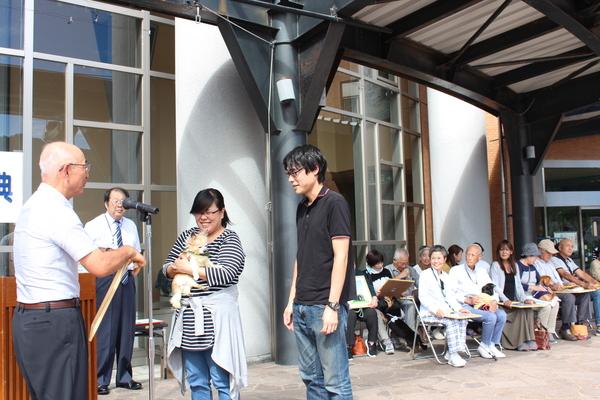 長寿犬を抱っこしている笑顔の飼い主夫婦が表彰されている写真