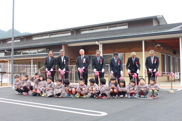 来賓の方がテープカットをしている前に園児が座っている写真