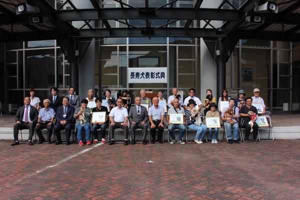 式典会場にて長寿犬と飼い主の方たちが表彰状を持って市長らと一緒に記念撮影している写真