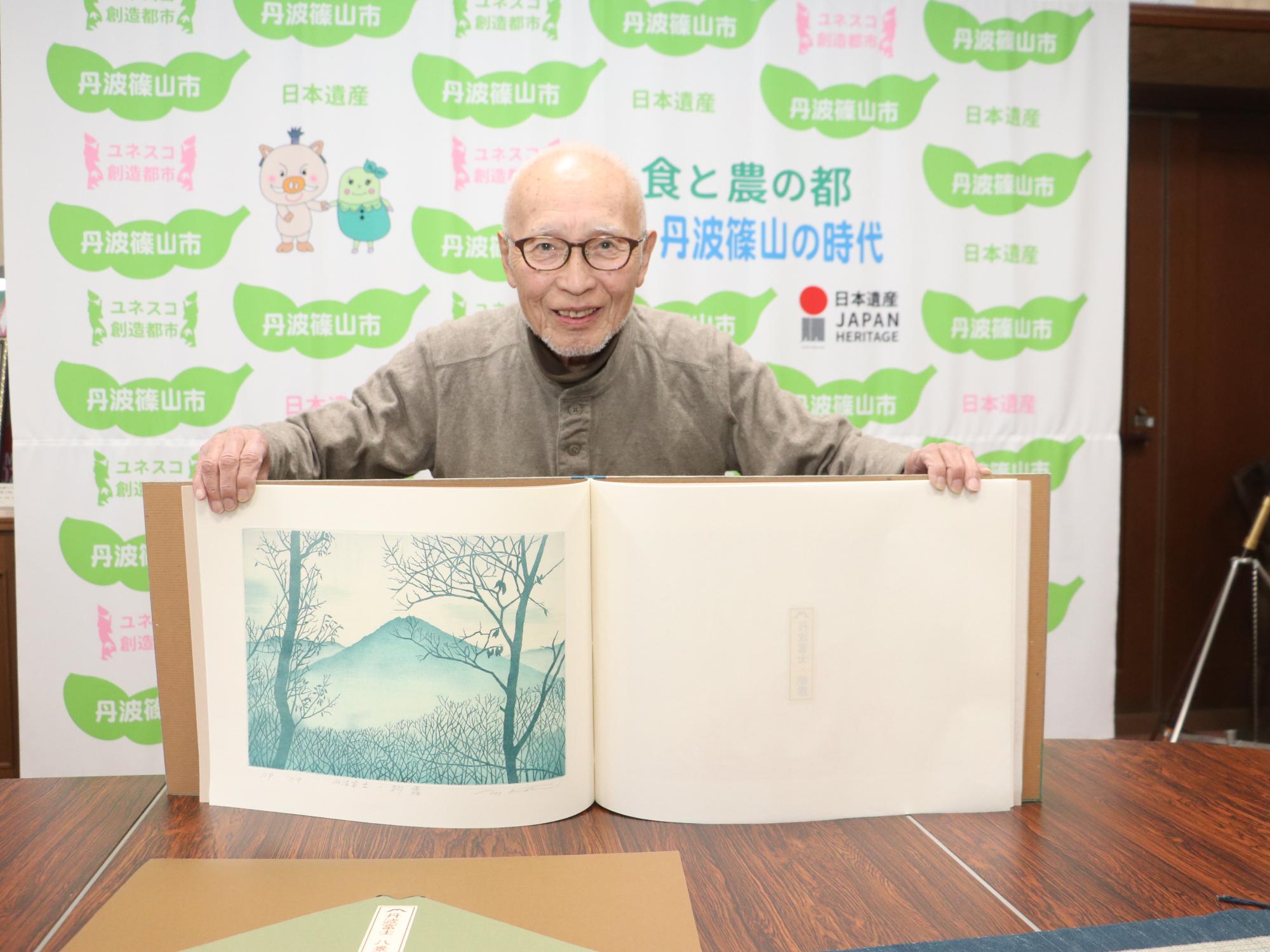 机の上で、作家が、版画集をひろげている