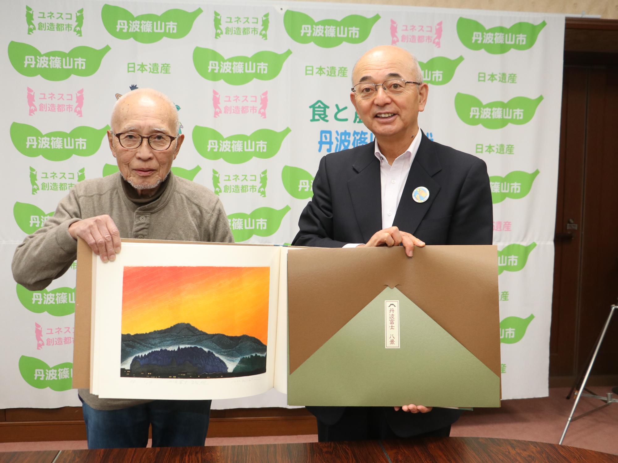 版画集を、作家の男性と市長が一緒に広げて持っている。