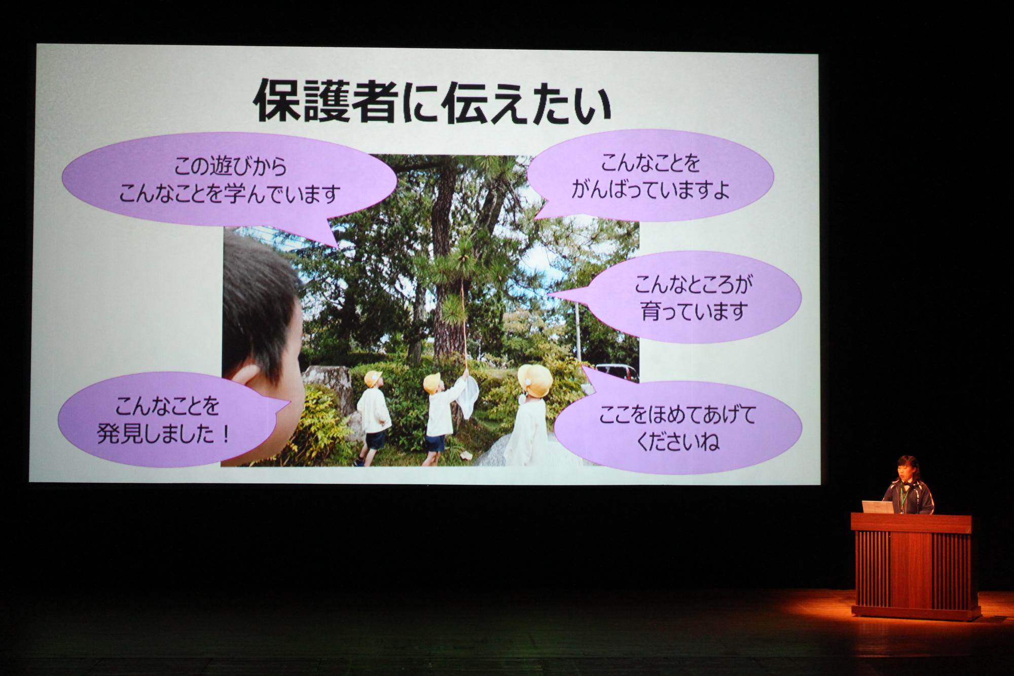 子どもたちが木の下で遊んでいる写真と「こんなところをがんばっていますよ」など保護者に伝えたいことをスライドに写し、その横で発表をする篠山幼稚園の先生