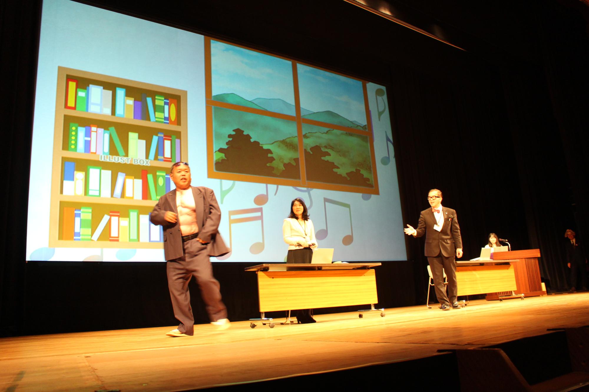 舞台で左に市民役の秘書課職員、真ん中の机の後ろに秘書、右に秘書課長がいて、市民役の職員が舞台のそでにはけようとしている写真