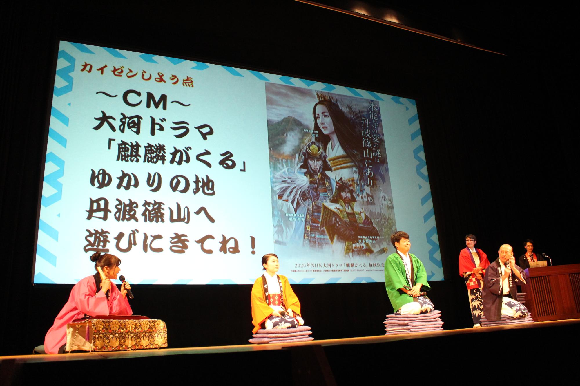 笹浴衣とピンクや黄色など色とりどりのハッピを着た職員が笑点のように座布団を何枚を敷いて話している様子。普段は商売の「商」の漢字で商工観光課ですが、今回は笑うの「笑」を使って笑工観光課として発表しています
