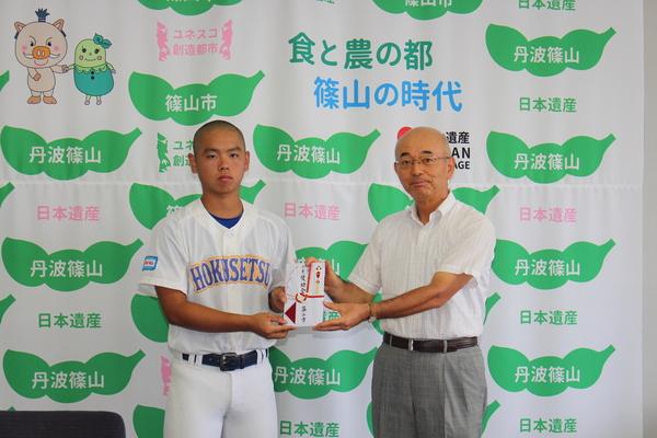 ユニホーム姿の中学生男子が市長と一緒に奨励金を持ってを記念撮影している写真