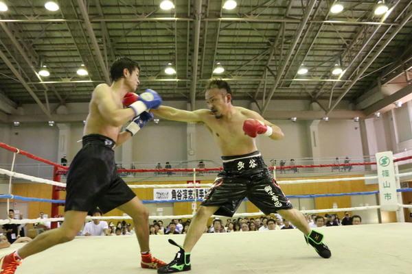 角谷選手がリングで相手にパンチしている壮行試合の写真