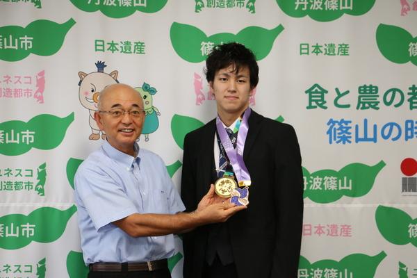 溝畑 樹蘭選手の首にかかる、2つのメダルを手にする市長の写真