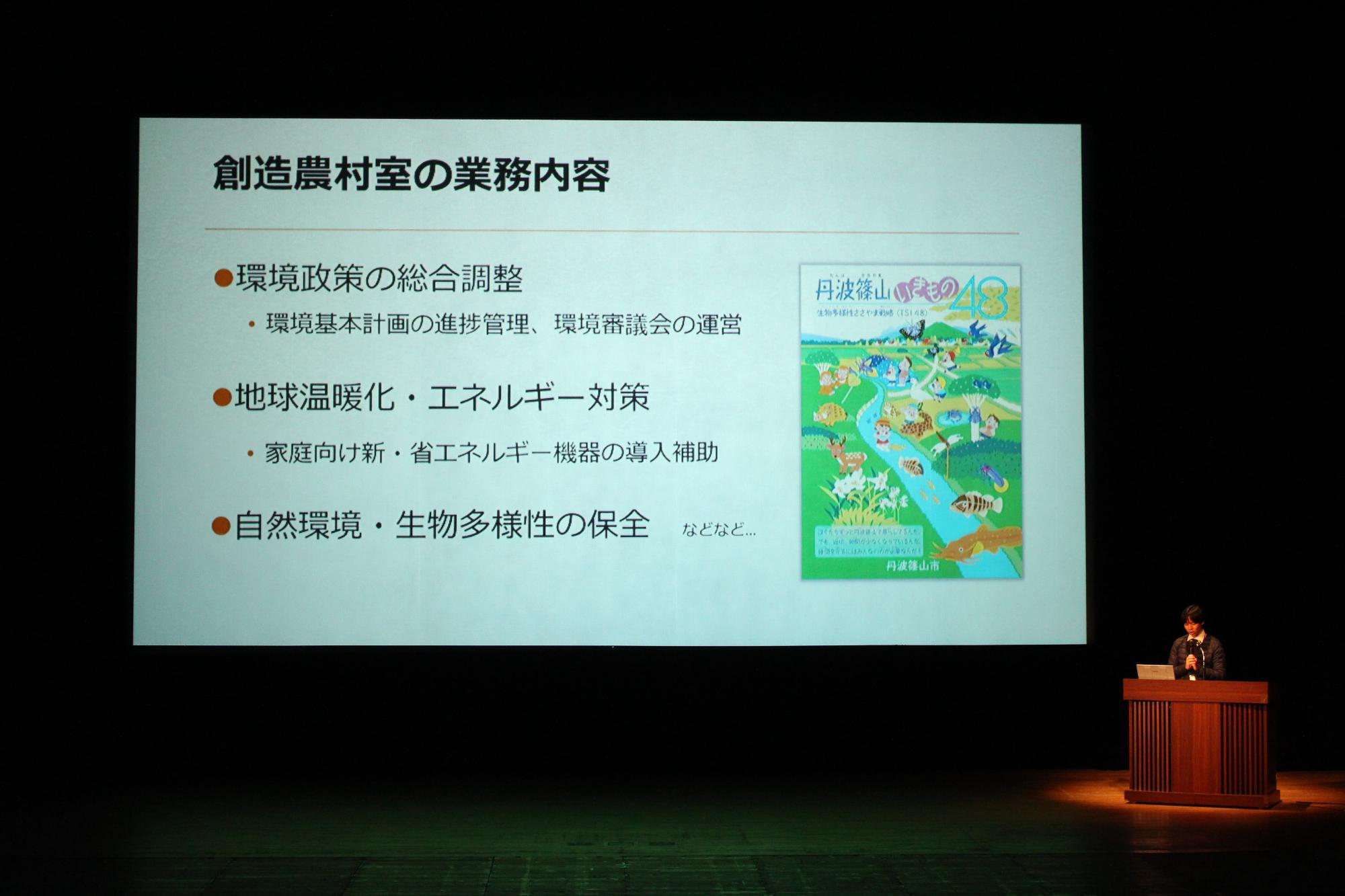 環境政策の総合調整など創造農村室の業務内容と書かれたスライドと、その説明をする創造農村室の男性職員