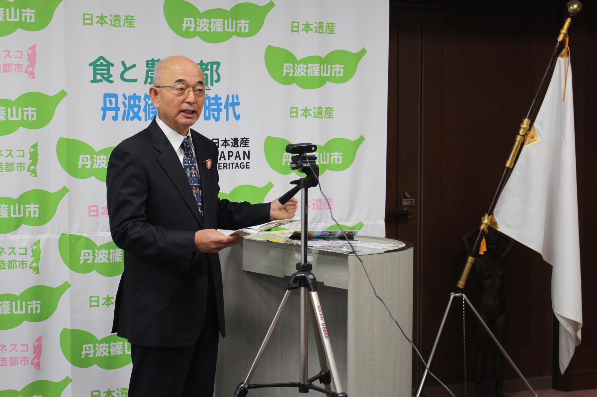 演台に資料を置いて、市長がモニターに向って説明している。